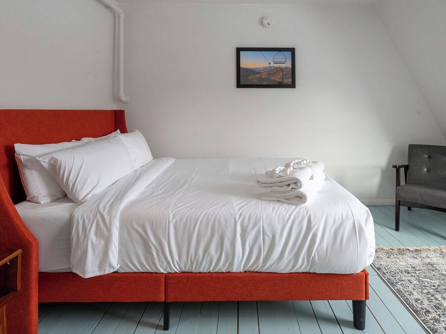 A neatly made bed with white linens, a red headboard, and a folded towel on the bed.