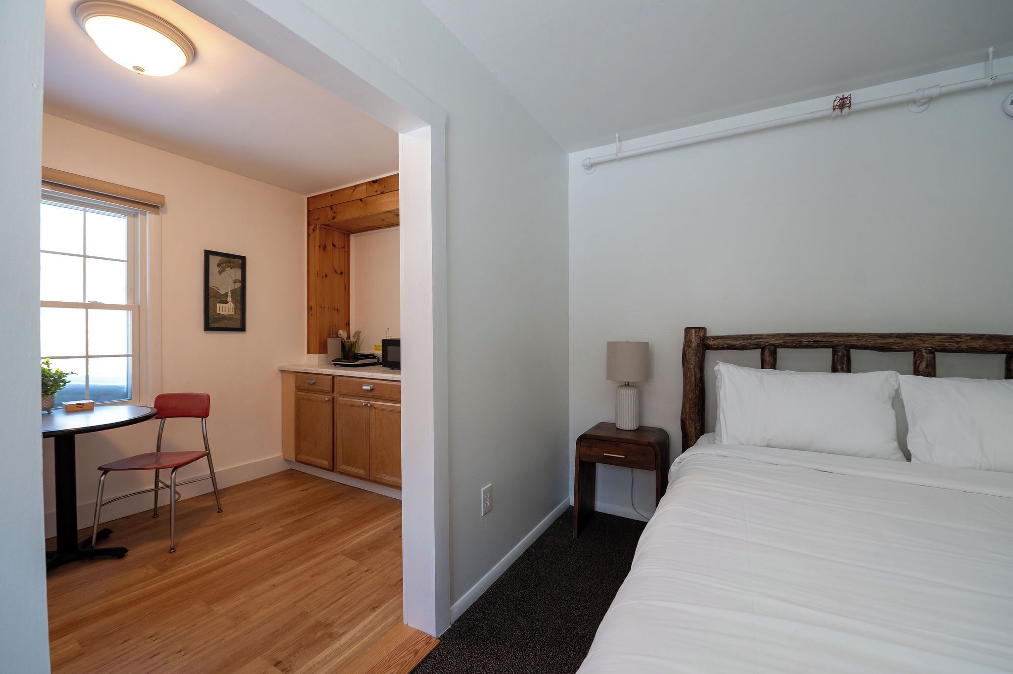 A bedroom with a wooden headboard, a bedside table with a lamp, and a small desk with a chair.