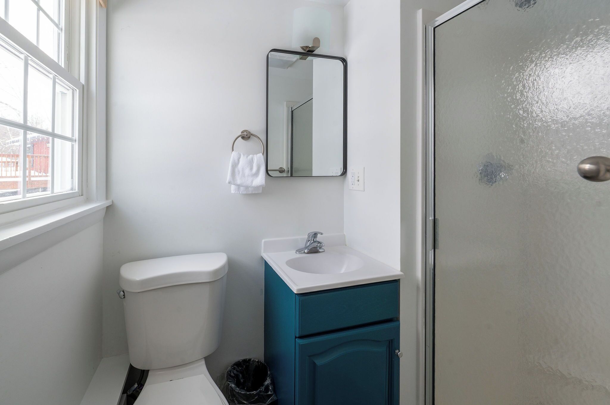 A bathroom with a white toilet, a teal vanity with a sink, and a mirror above the vanity.