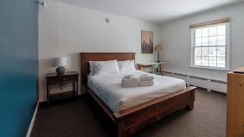 A bedroom with a wooden bed, a nightstand, a desk, a lamp, and a window.