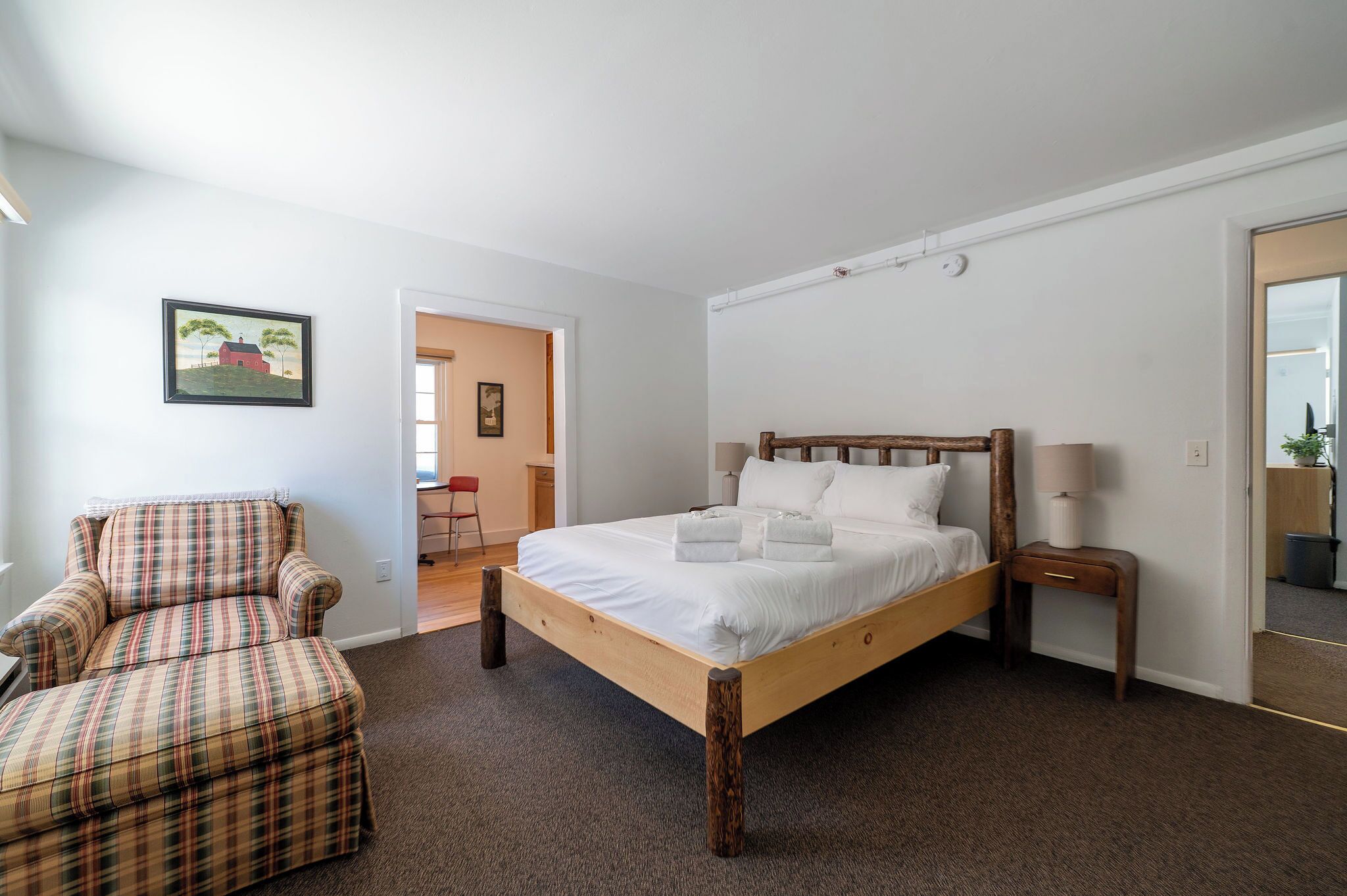 A bedroom with a wooden bed, a plaid armchair, and a small bedside table.
