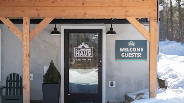 A wooden structure with a black door labeled "KILLINGTON HAUS GUEST ENTRANCE" and a sign saying "WELCOME GUESTS!". - Killington Haus (Killington)