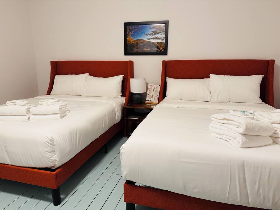 Two twin beds with white linens and red headboards, a nightstand with a lamp and a framed picture on the wall.