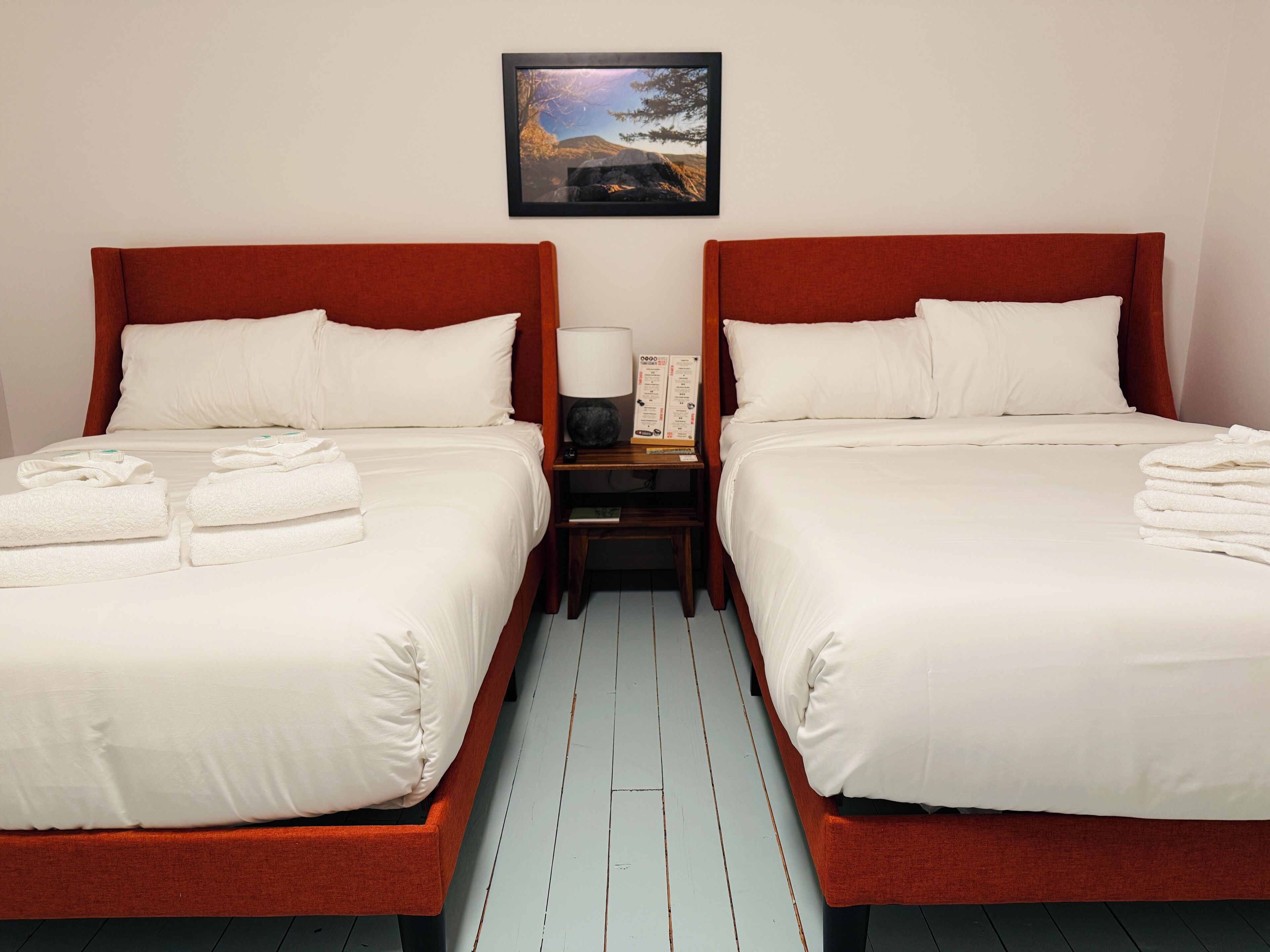 Une chambre d’hôtel avec deux lits, du linge de lit blanc et un tableau encadré au mur.