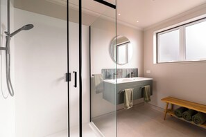 Une salle de bain moderne avec une douche à parois de verre, un meuble-lavabo à deux vasques, un miroir rond et un banc avec des serviettes.