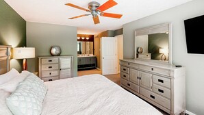 Une chambre à coucher comprenant un lit, une commode, une coiffeuse et un ventilateur de plafond.
