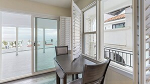 En balkon med glasdør, spisebord med stole og udsigt til havet.
