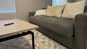 A living room with a grey sofa, patterned cushions, a wooden coffee table, and a patterned rug. - Pool, A+ location, washer/dryer, LongStayDiscounts (Sherman)