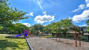 A playground with a blue slide, red climbing structure, and a swing set. - Pool, A+ location, washer/dryer, LongStayDiscounts (Sherman)
