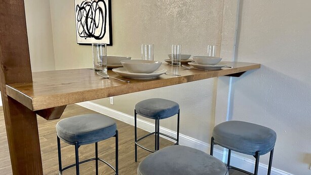 A modern kitchen with a wooden countertop, three bar stools, and a wall-mounted shelf with bowls and glasses. - Pool, A+ location, washer/dryer, LongStayDiscounts (Sherman)