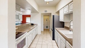 A narrow kitchen with white cabinets, a microwave, and a refrigerator. - Dog-Friendly Home w/ Fenced Yard in Sierra Vista! (Sierra Vista)