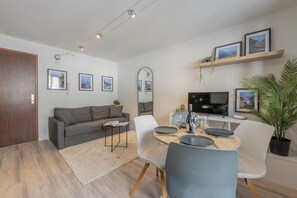 A modern living room with a sofa, coffee table, dining table, chairs, TV, and framed pictures on the wall. - Alpine Flégère, 1BR Near Flégère Lift, Chamonix, France (Chamonix)