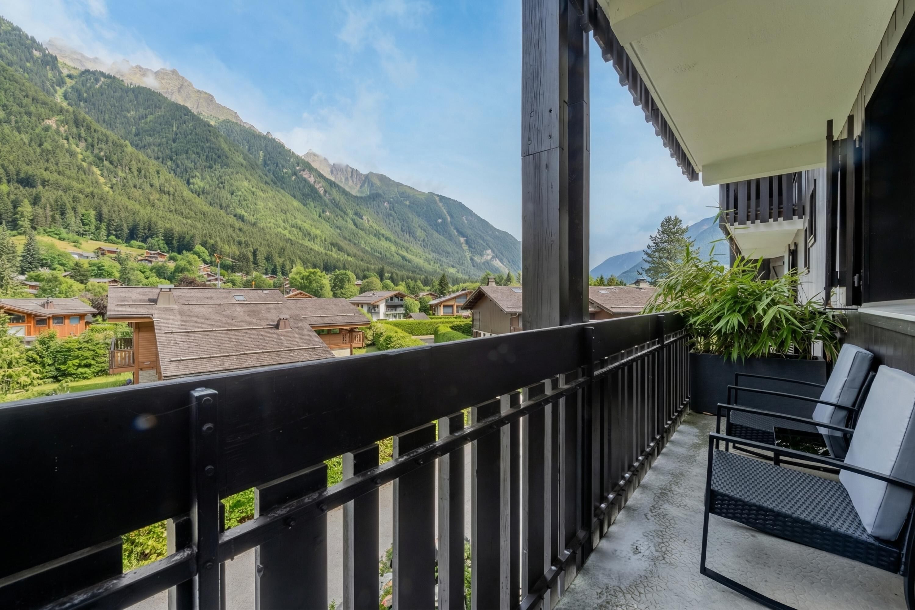 A balcony with a view of a mountainous landscape, a wooden building, and a potted plant.