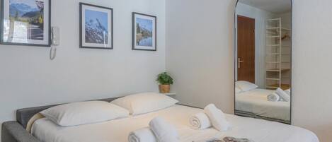 Un llit ben arriscat amb llençols blancs i tovalloles esteses, una planta a la nitriera i un mirall que reflecteix l'habitació.