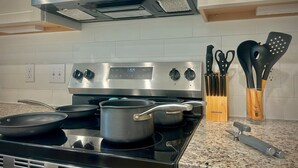 Une cuisine équipée d’une cuisinière en acier inoxydable, d’un four à micro-ondes placé au-dessus, et d’un ensemble de couteaux et de spatules rangés dans un porte-ustensiles en bois.