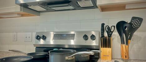 A kitchen with a stainless steel stove, a microwave above it, and a set of knives and spatulas in a wooden holder.