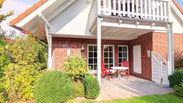 A two-story house with a balcony, a patio with outdoor furniture, and a brick exterior. - Ferienhaus in Burhave (Butjadingen)