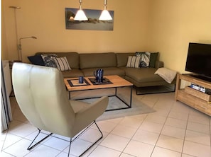 A living room with a sofa, a coffee table, a chair, a television, and a painting on the wall. - Ferienhaus in Burhave (Butjadingen)