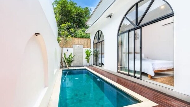 A modern pool area with a clear pool, wooden deck, and a bed with a white bedspread. - Villa Eclipse B2 (Jimbaran)