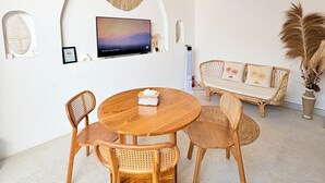 A dining area with a round wooden table and four wicker chairs, a sofa with cushions, and a mounted television on the wall. - Villa Eclipse B2 (Jimbaran)