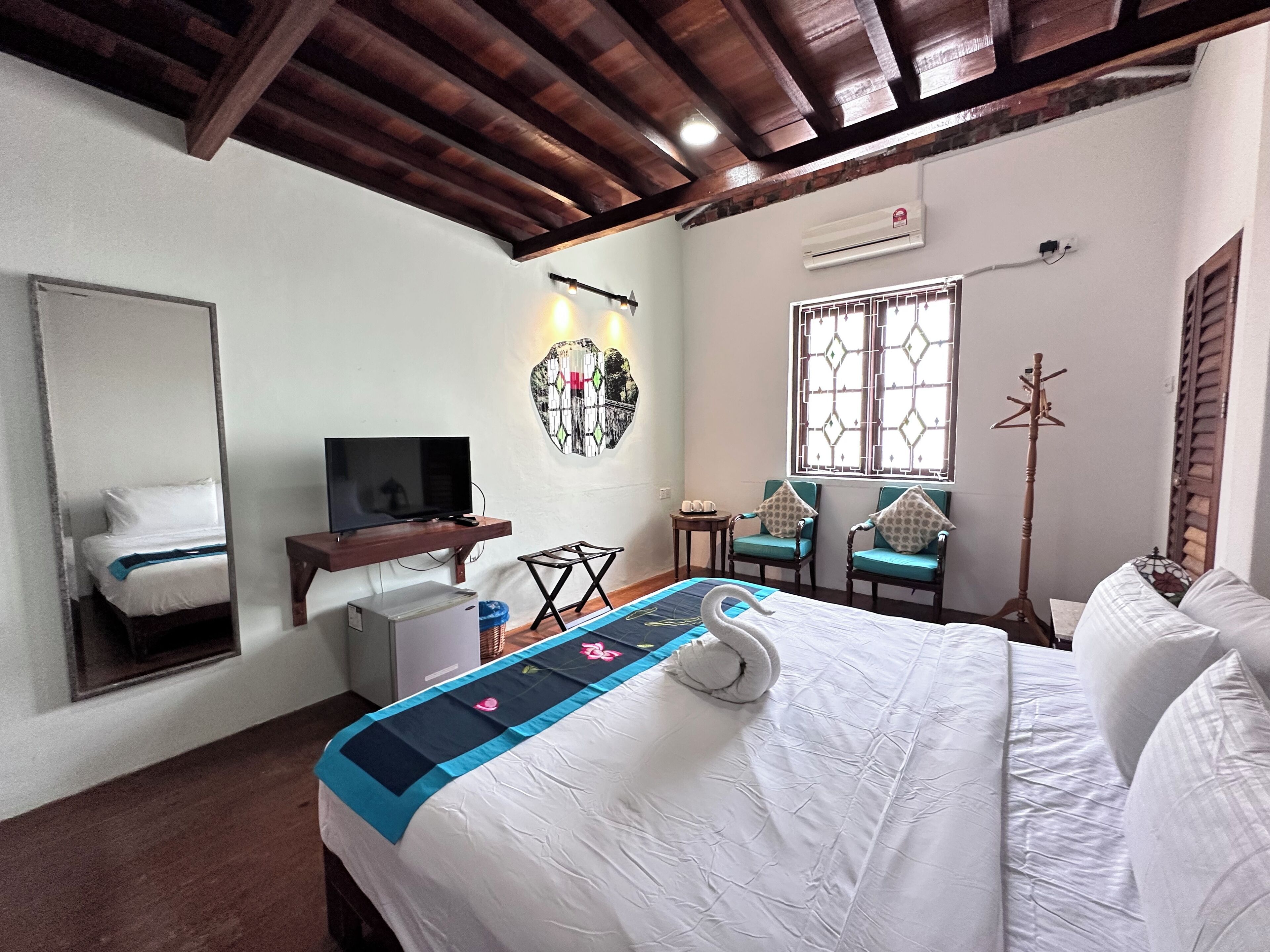 A hotel room with a bed, a TV, a wall-mounted air conditioner, and a window with decorative shutters.
