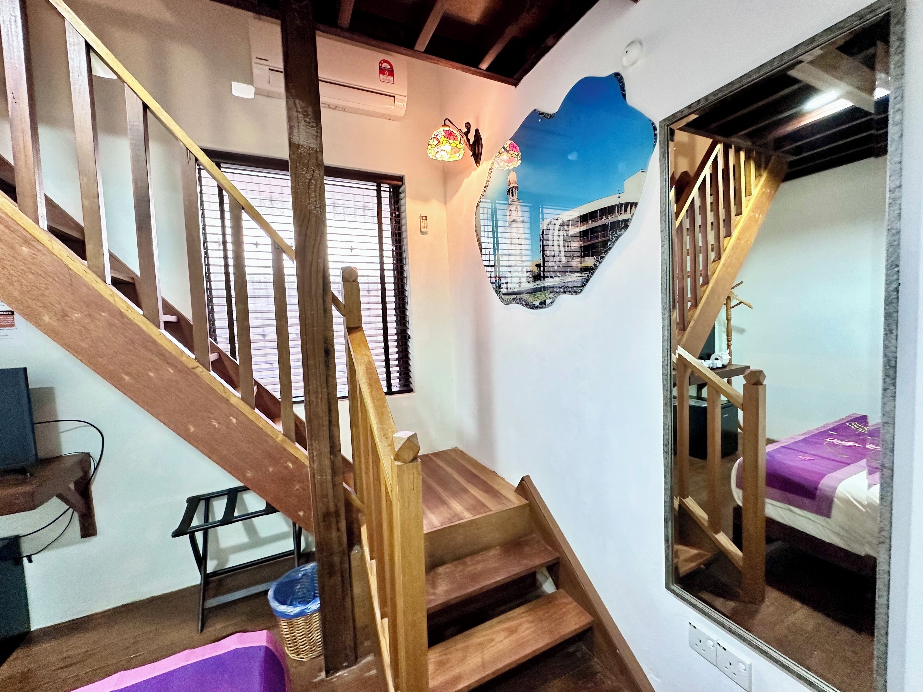 A staircase with wooden railings and a mirrored wall reflecting a bed with a purple blanket.