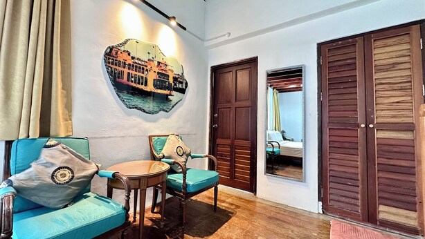 A room with a wooden floor, two blue armchairs, a small round table, a wall-mounted mirror, and a door with a wooden panel. - Rangoon Residence 26 (George Town)