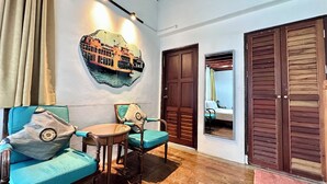 Une pièce avec un plancher en bois, deux fauteuils bleus, une petite table ronde, un miroir fixé au mur et une porte avec un panneau en bois.
