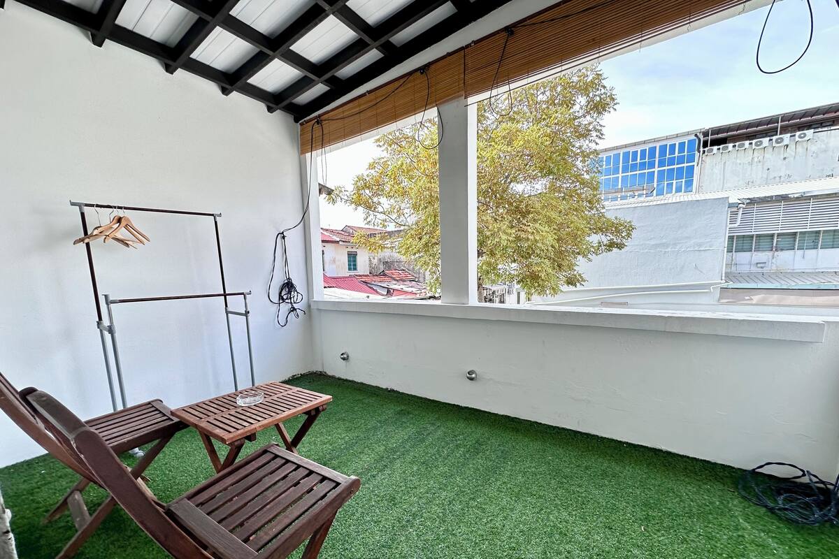 A balcony with artificial grass, two wooden chairs, a small table, and a view of buildings and trees.