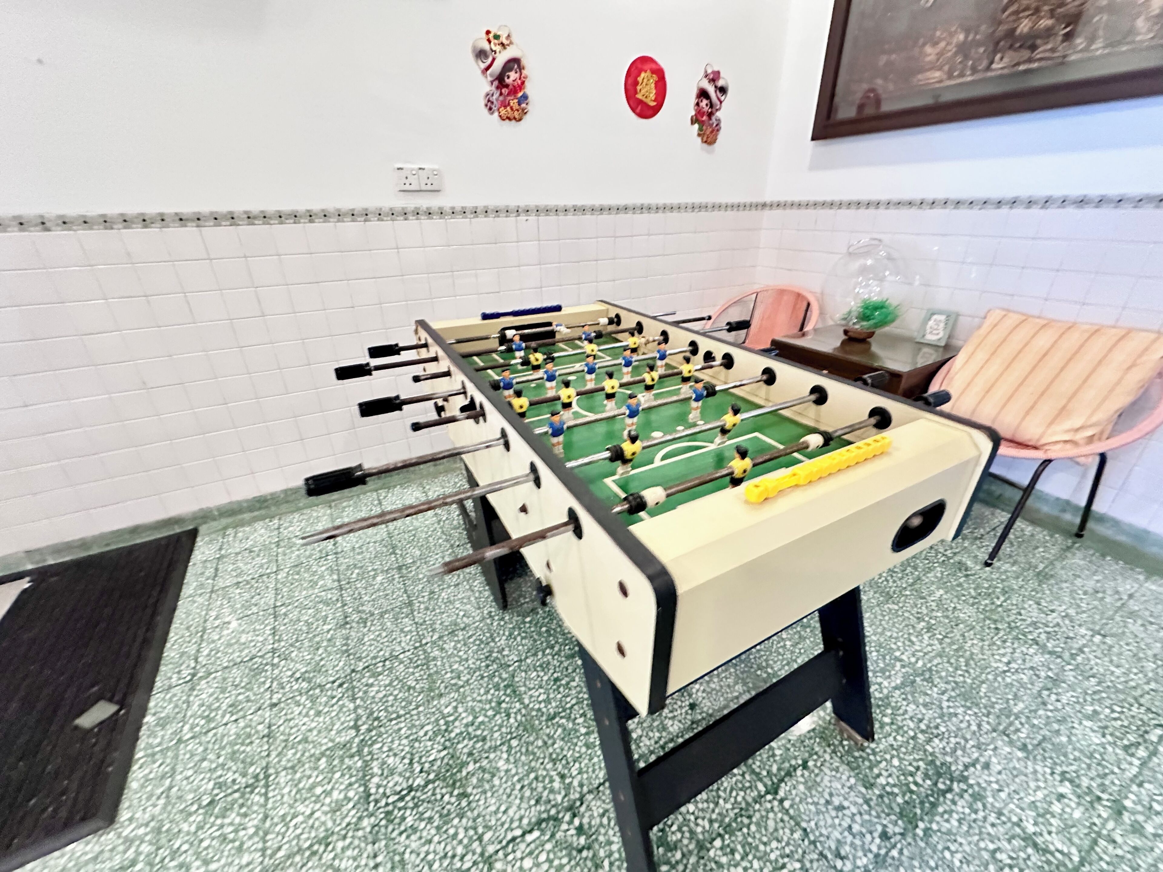 A foosball table in a room with tiled walls and a green floor.
