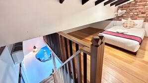 A bedroom with a wooden bed, a brick wall, and a view of a tower through a window. - Rangoon Residence 26 (George Town)