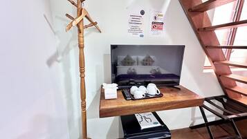 A hotel room with a wooden coat rack, a flat-screen TV, a tray with cups and a remote, and a black Hisense air purifier.