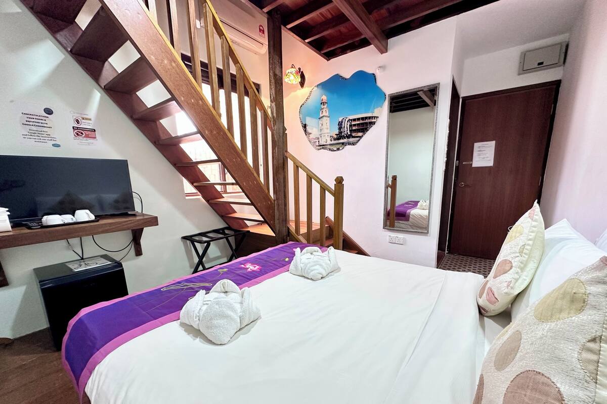 A hotel room with a bed, a TV, a desk, a staircase, and a mirror.