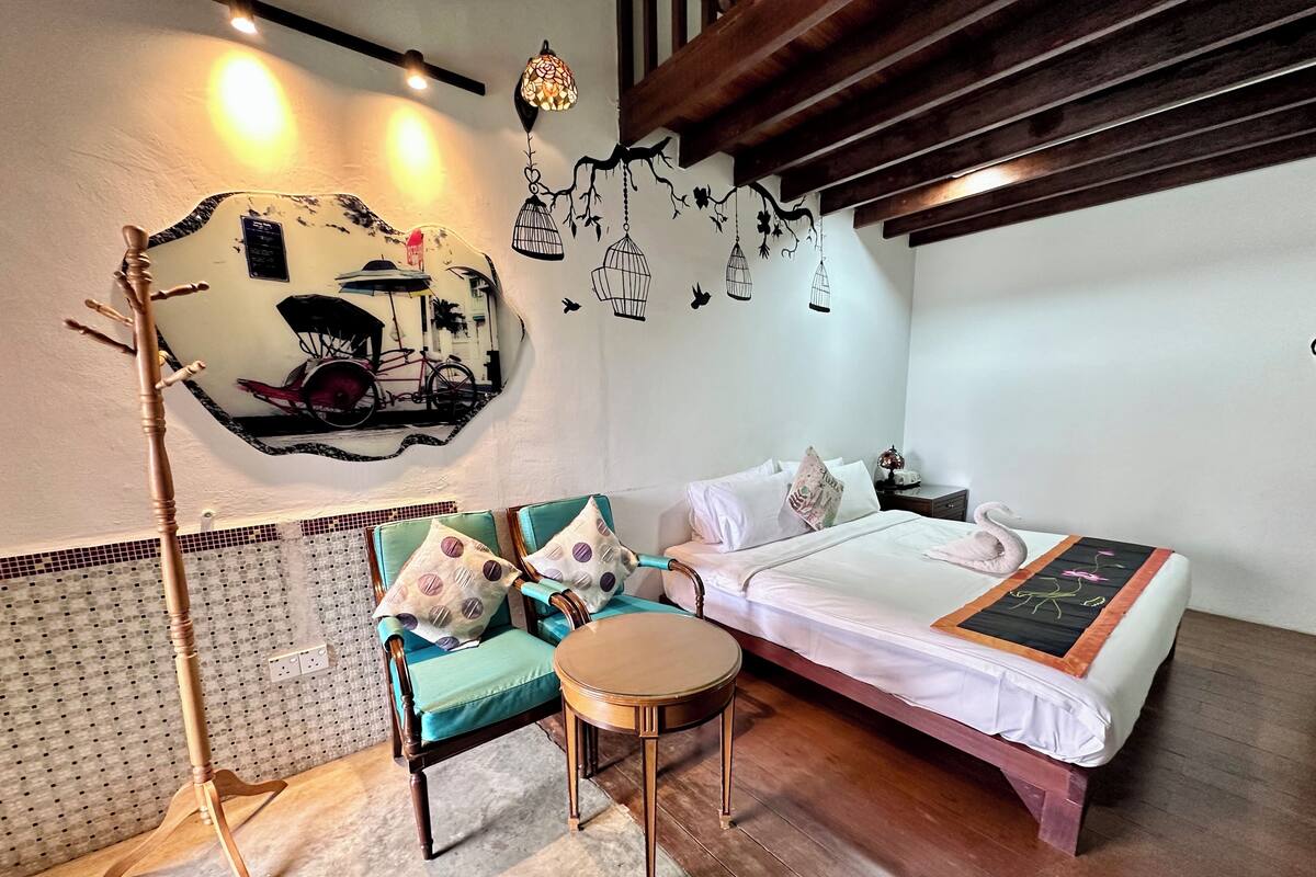 A cozy room with a bed, two chairs, a small table, and a decorative wall with a bicycle and a bird mural.