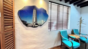 A room with a large wall mural of a cityscape, wooden shutters, and two blue chairs. - Rangoon Residence 26 (George Town)