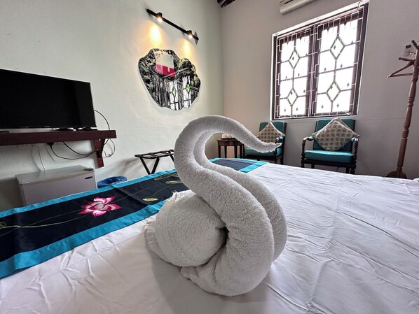 A hotel room with a bed, a television, a wall-mounted artwork, a window with a decorative grille, and two chairs. - Rangoon Residence 26 (George Town)