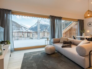 Un salon moderne doté d’une grande fenêtre donnant sur un paysage montagneux enneigé.