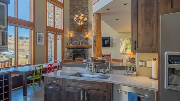 A modern kitchen with a stone fireplace, large windows, and a dining area with colorful chairs. - Ski-in/ski-out 4-bedroom townhome in Crested Butte! (Gunnison)