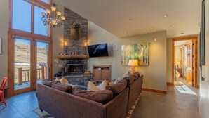 A spacious living room with a stone fireplace, a large flat-screen TV, and a comfortable sectional sofa. - Ski-in/ski-out 4-bedroom townhome in Crested Butte! (Gunnison)