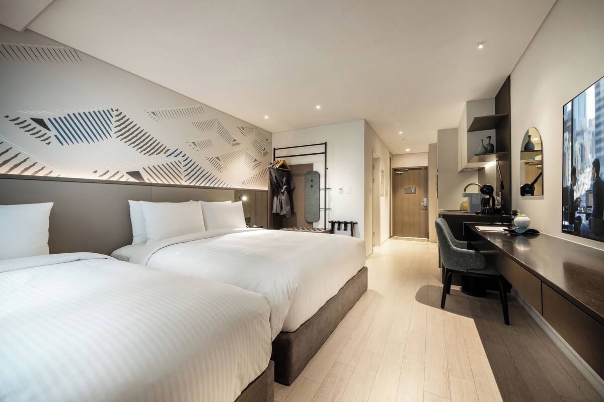 Een moderne hotelkamer met twee bedden, een bureau en een grote spiegel.