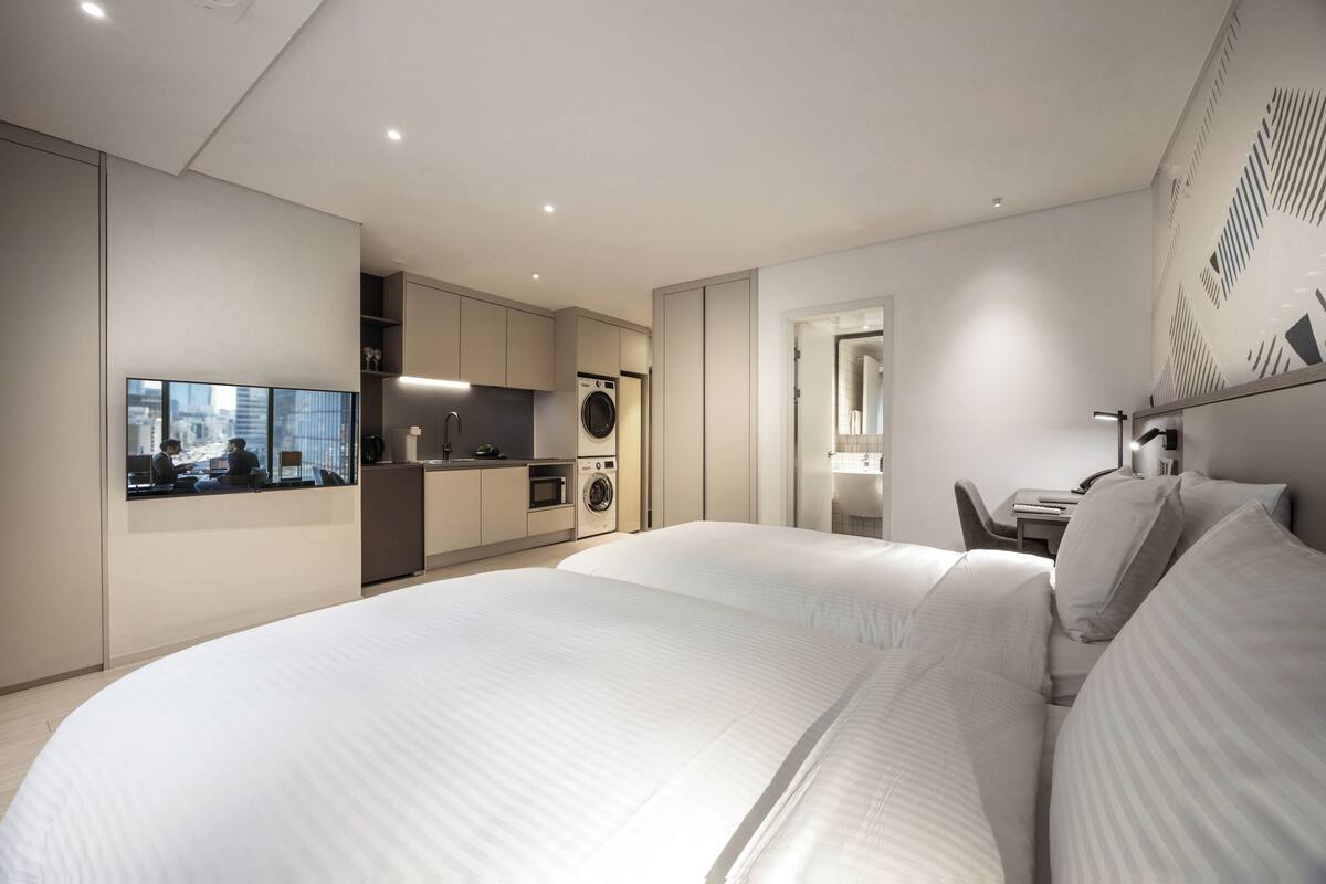 Een moderne hotelkamer met een groot bed, uitzicht op de stad, een kitchenette en een badkamer.