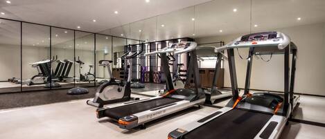 A modern gym with treadmills, ellipticals, and a mirrored wall.