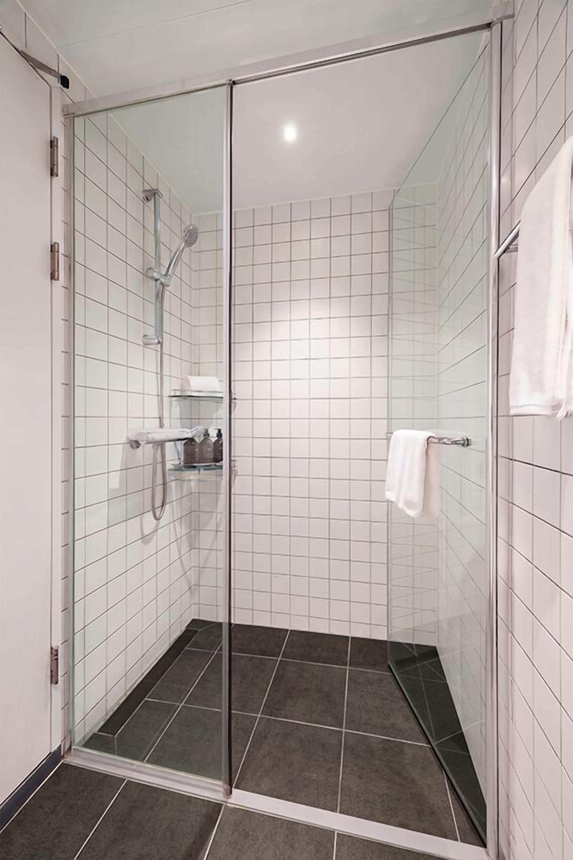 A glass-enclosed shower room with white tiled walls and a dark floor.