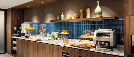 Una cocina moderna con estación de café, presentación de alimentos y contenedores de basura señalizados para residuos generales y reciclaje.