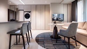 Una habitación de hotel moderna con zona de comedor, sofá, televisor y lavadora.