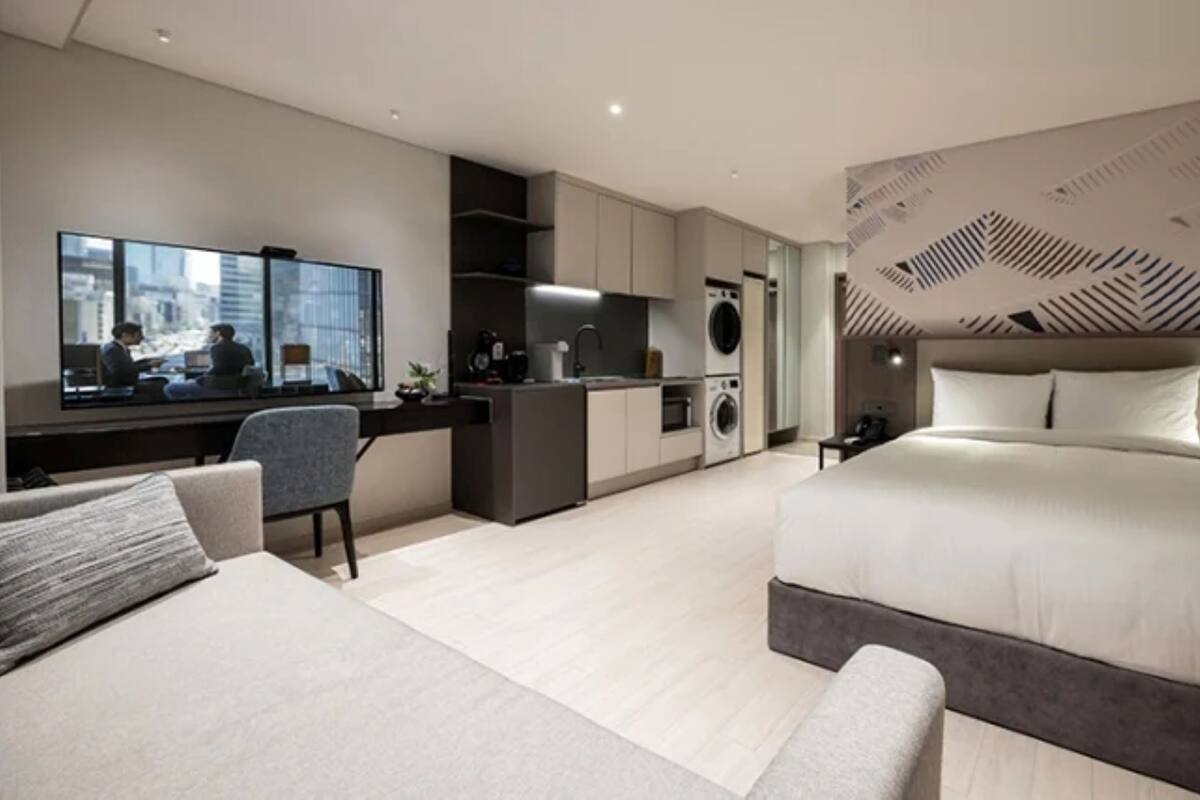 Een moderne hotelkamer met een groot bed, een bureau, een zithoek, een kitchenette en uitzicht op de stad.