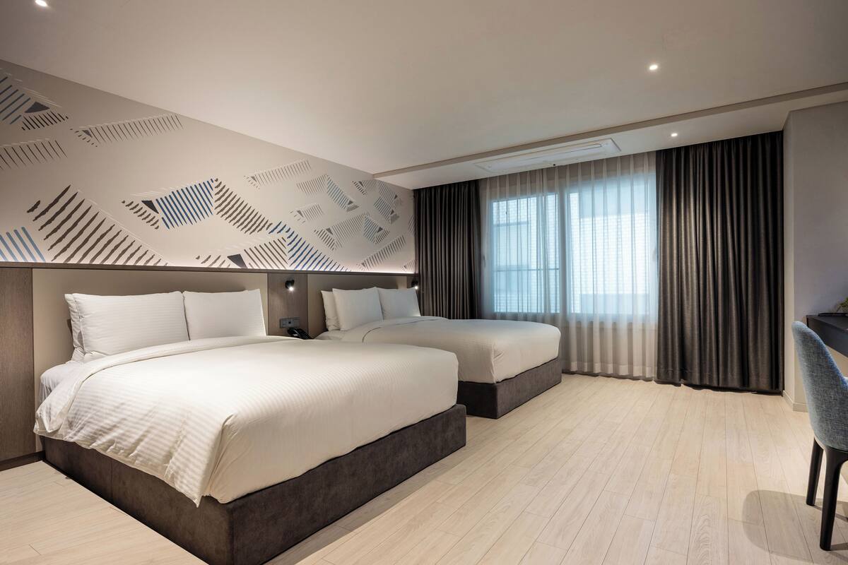 Een hotelkamer met twee bedden, een bureau en een groot raam met gordijnen.