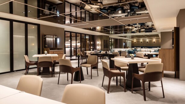 Un interior moderno con varias mesas y sillas para comer, una zona de cocina y una escalera que conduce a un nivel superior.