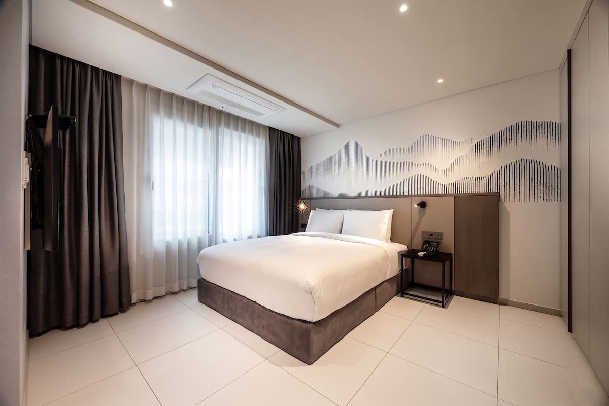 Een moderne hotelkamer met een groot bed, een nachtkastje, een wandairconditioner en een decoratief wandpaneel.