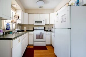 Una cucina compatta con mobili bianchi, un forno a microonde, un forno e un frigorifero.